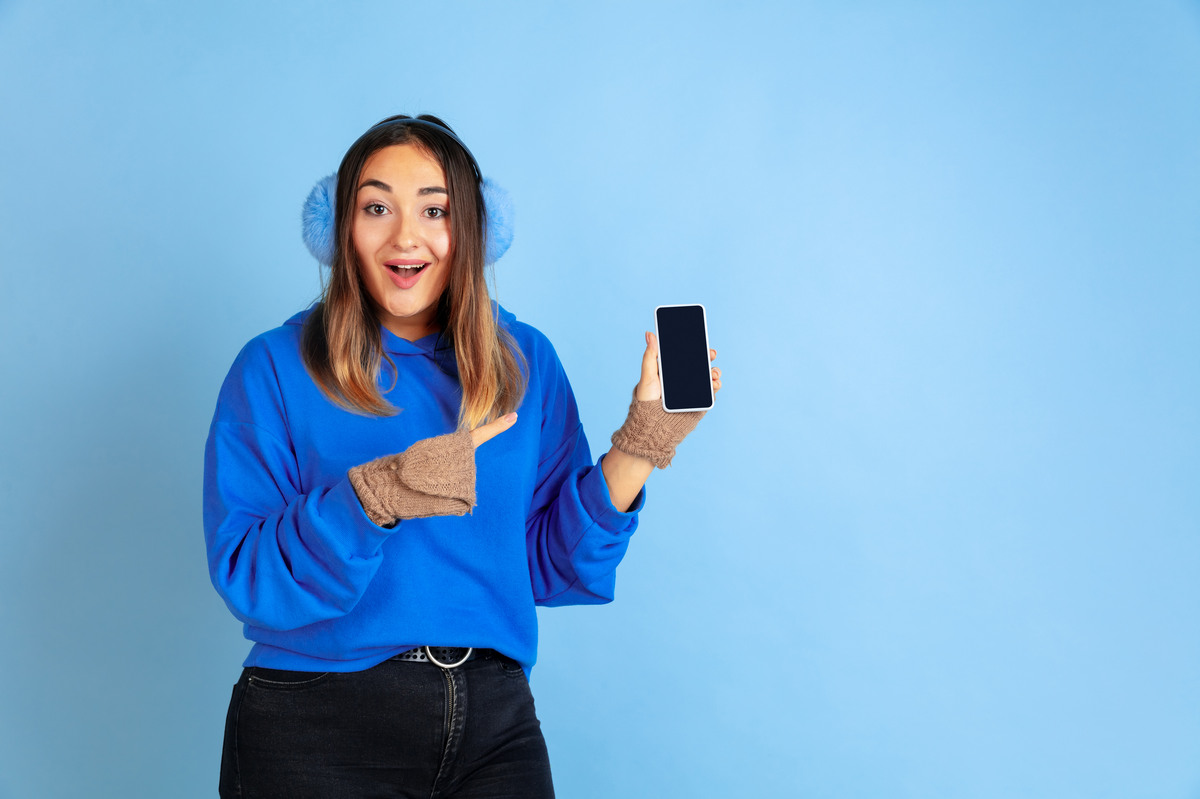 Femme en bleu montre son smartphone du doigt, ravie de son forfait 30 Go de Cdiscount Mobile à 5€